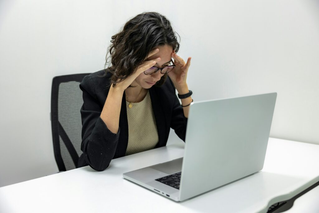 Woman with a tension headache holding her temples while working at a laptop – chiropractic headache relief in Dothan, AL